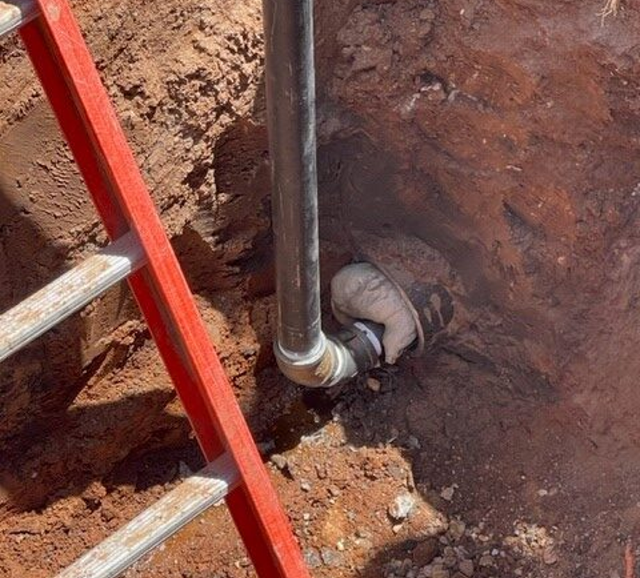 Exposed underground pipe and elbow in an excavated soil area beside an access ladder