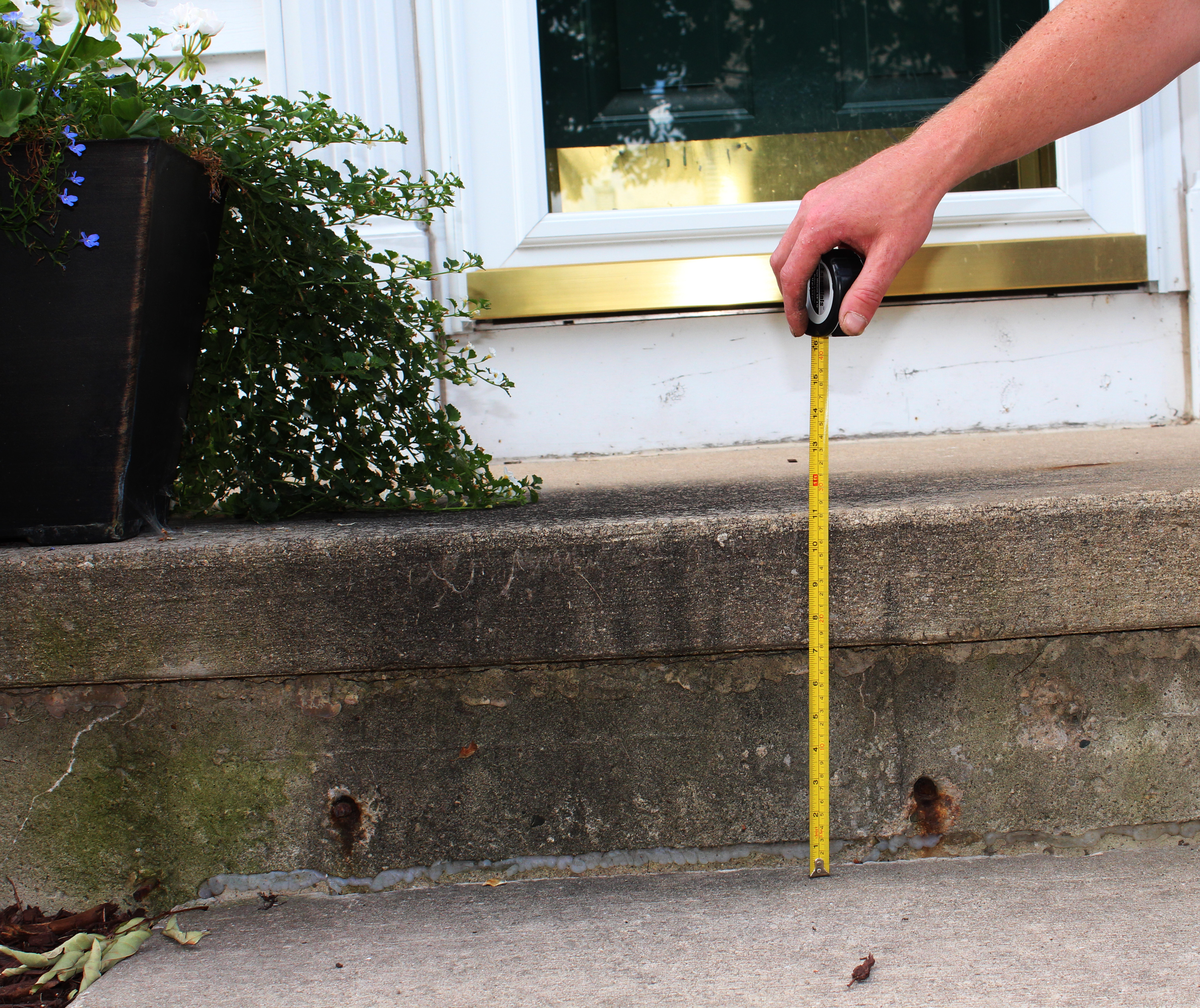 Person measuring concrete step settlement gap at front door in Houston Texas showing slab sinking